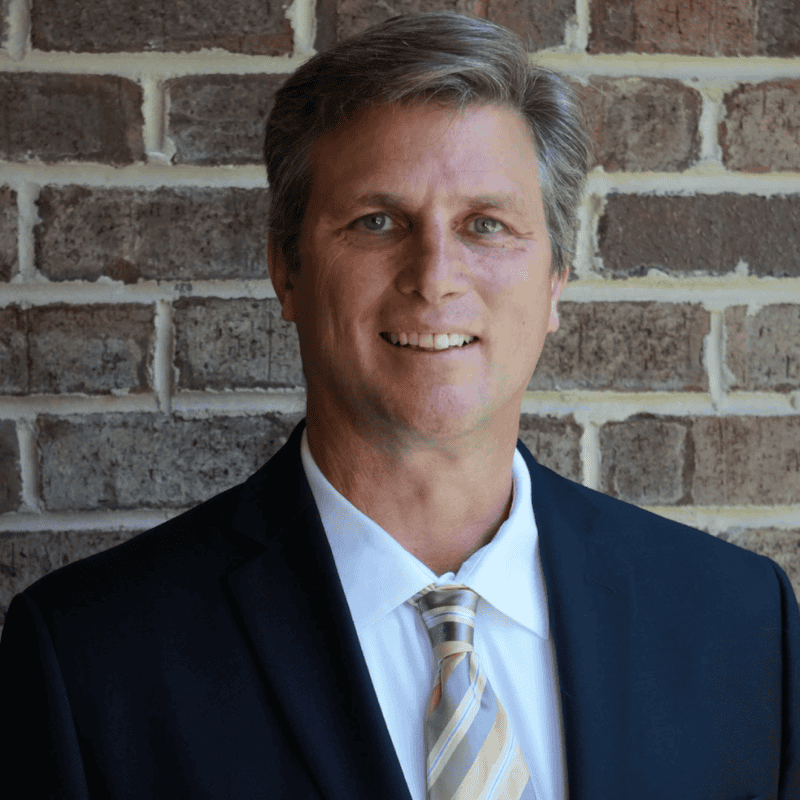 Man in suit standing against brick wall.